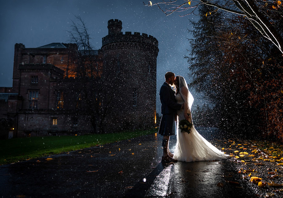 Bride and groom evening kiss in the rain with the shadow of Dalhousie Castle in background